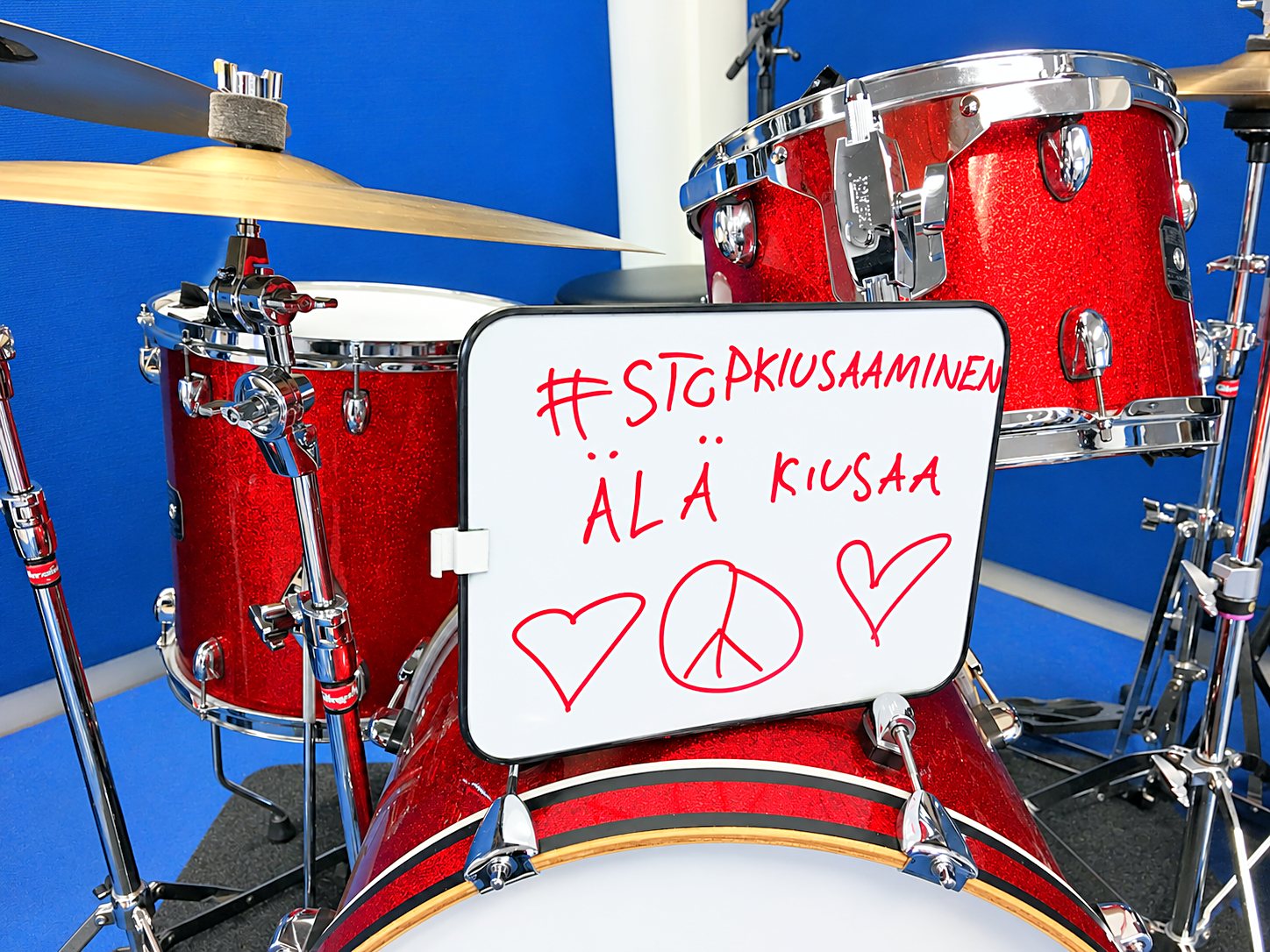 A sign in front of a drum kit: #stopkiusaaminen – Älä kiusaa (Don’t bully), with hearts and a peace sign